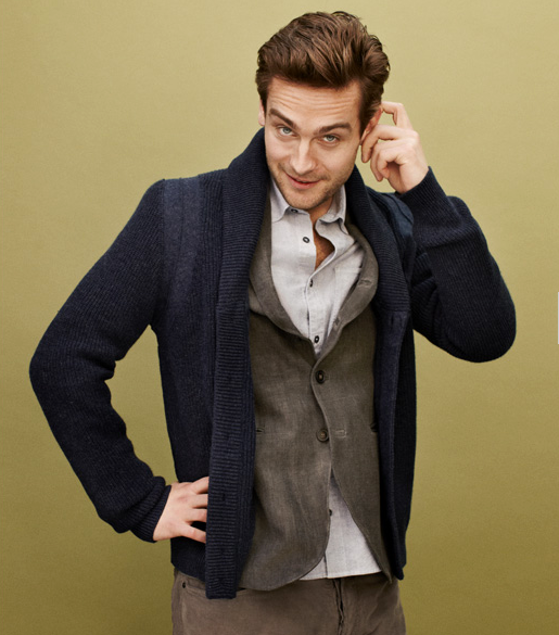 Tom Mison in a blue cardigan scratching his ear